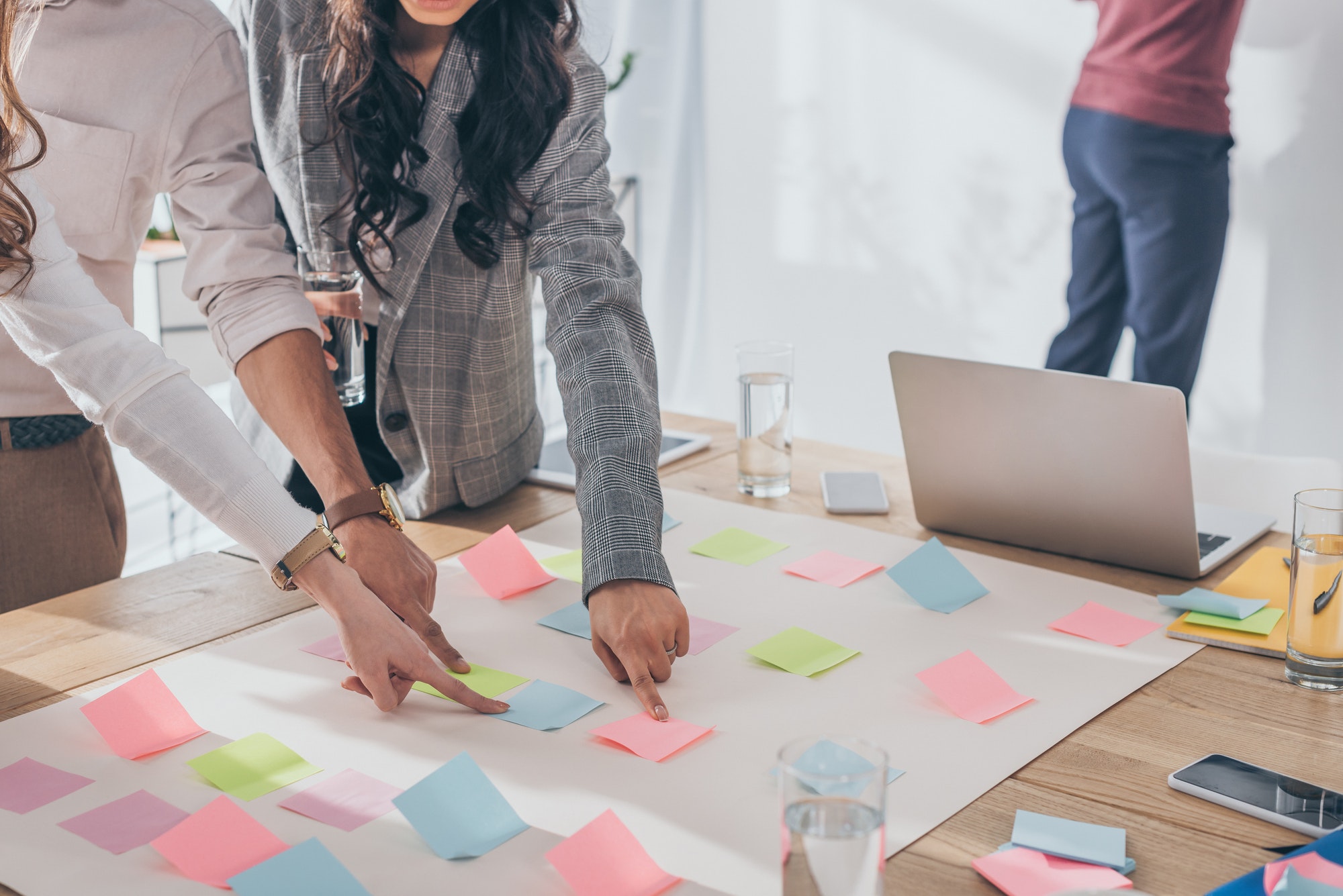 cropped view of businesswomen and businessman pointing with fingers at sticky notes